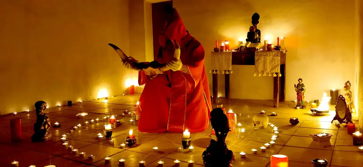 Il Maestro in tunica rossa regge le corna rituali davanti all'altare