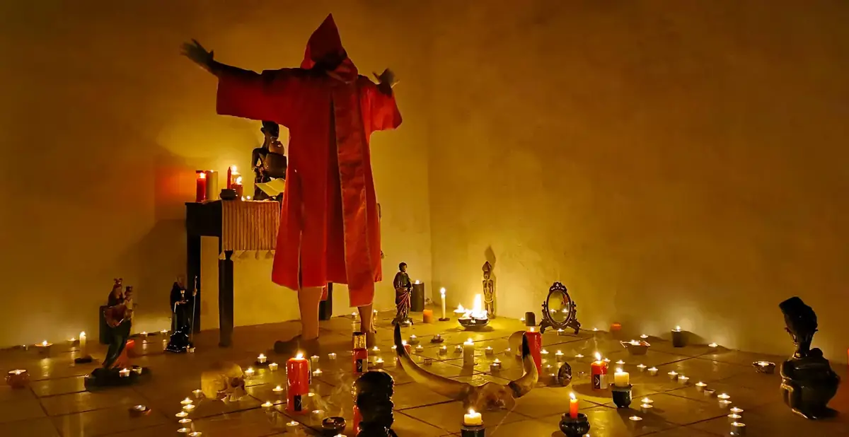 Il Maestro in tunica rossa a braccia aperte nel cerchio di candele